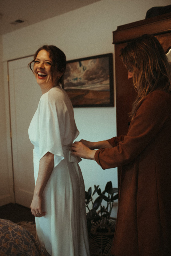 a woman helping her sister into her bridal gown