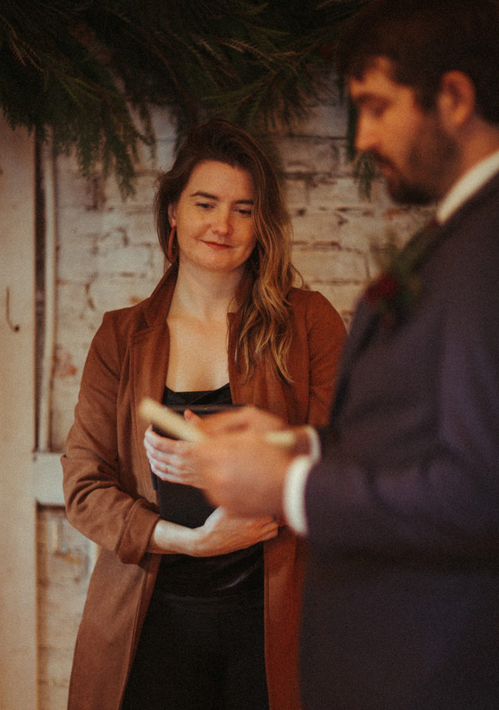 the officiant smiling as the groom reads his vows
