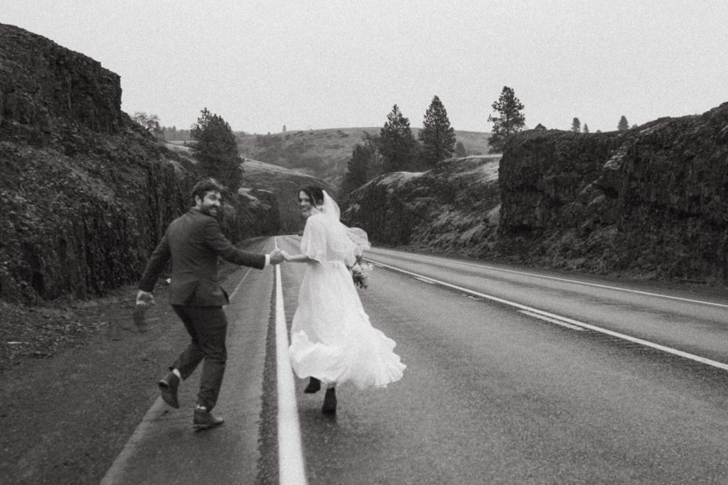 couple running across a highway in the columbia river gorge after eloping