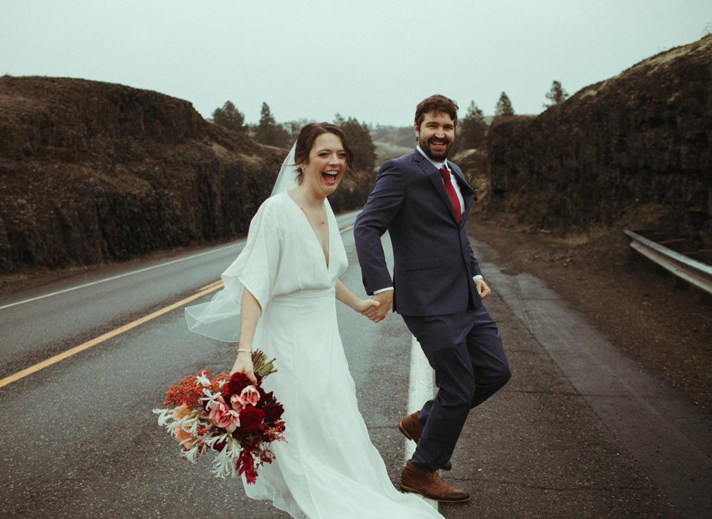 couple running across a highway in the columbia river gorge after eloping