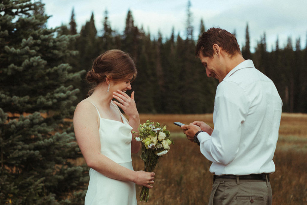 bride wipes away a tear while her groom reads his vows in this intimate elopement near mt. adams