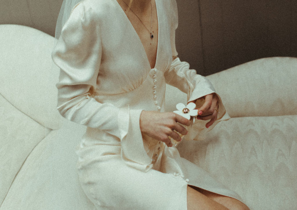 bride holds her daisy perfume while sitting on a sofa before her wedding in vancouver washington