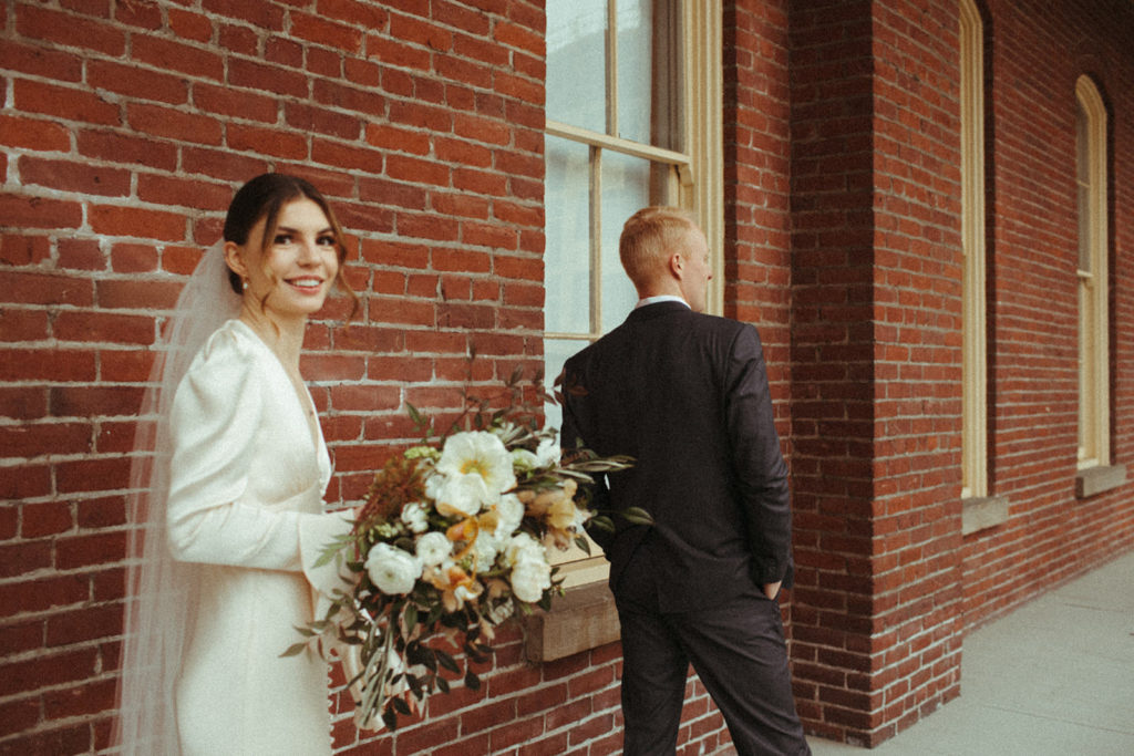 bride smiles back just before sharing her first look with her groom outside of the Academy venue in Vancouver Washington