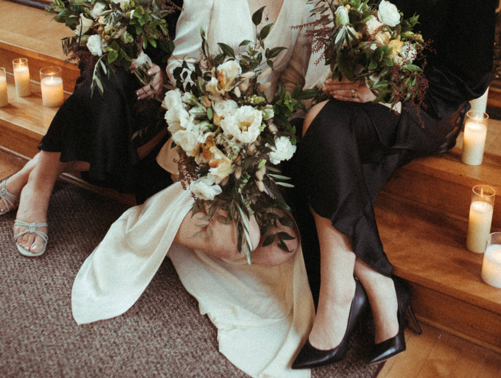 the bride and bridesmaids hold their bouquets in their laps on the steps of the chapel at the Academy